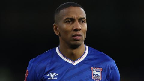 Ashley Young, wearing Ipswich Town's blue home shirt with a white collar and red and blue trim. The shirt has an Umbro logo on one side and Ipswich crest on the other.