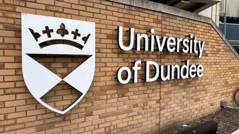 A sign saying University of Dundee affixed to a brick wall