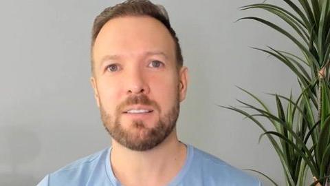 Barclay Littlewood has ginger hair and a beard and wears a light-blue top. A tall green pot plant sits behind his left shoulder.