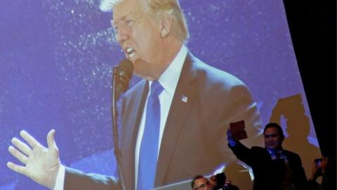 US President Donald Trump appears on a large video screen as he delivers remarks at the APEC CEO Summit in Danang, Vietnam on 10 November 2017