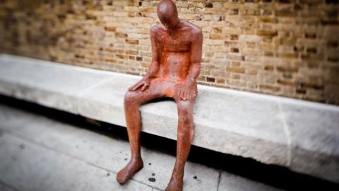 Life-sized sculpture sitting on a concrete bench