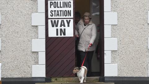 A woman walking her dog out of a polling station