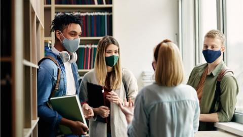 Group of college friends talking in library and wearing face masks due to coronavirus pandemic. - stock photo