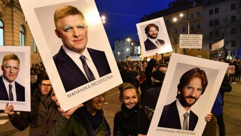 Protesters carry signs depicting Prime Minister Robert Fico, left, and interior minister Robert Kalinak