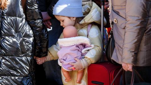 A little girl holding a woman's hand clutches a doll at the Uzhhorod-Vysne Nemecke checkpoint on the Ukraine-Slovakia border