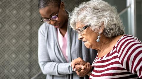 A stock image of an elderly woman being supported by a carer as she walks