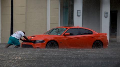 A man pushes a car through flood waters.