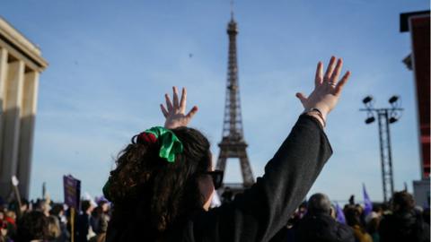 A woman raises her hands as people gather at the Place du Trocadero near the Eiffel Tower in Paris, on March 4, 2024, during the broadcasting of the convocation of both houses of parliament to anchor the right of abortion in the country's constitution.