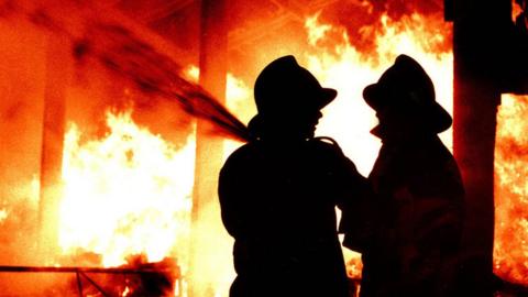 Firefighters in silhouette tackle a blaze