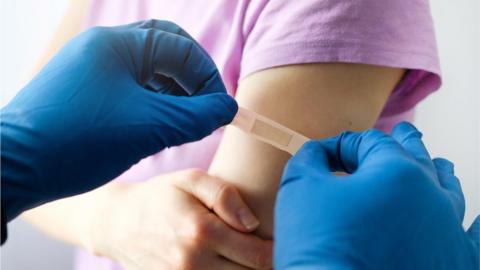 A vaccinator applies an adhesive bandage to a girl after vaccination