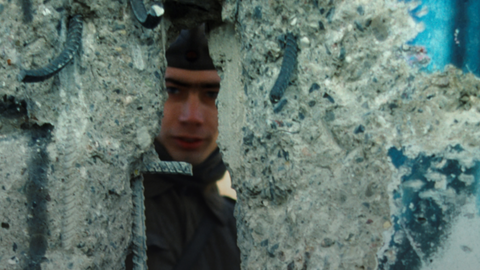 An East German guard peers through a hole in the Berlin Wall