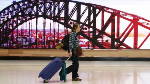 A traveller walking past a display screen showing the Sydney Harbour Bridge in Sydney Airport in March 2020