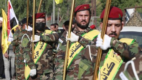 Fighters lift flags of Iraq and paramilitary groups, including Kataib Hezbollah, during a funeral in Baghdad for five militants killed in a US strike in northern Iraq, on 4 December 2023