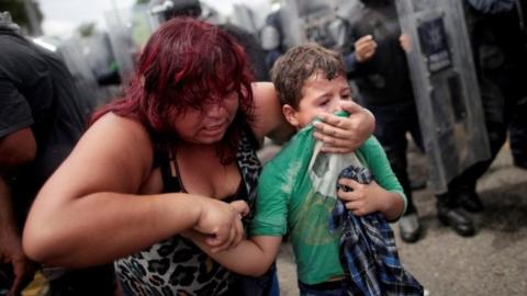A woman covers her young son's mouth with his tshirt. Tear gas was fired by Mexican police as they tried to force back the crowd.
