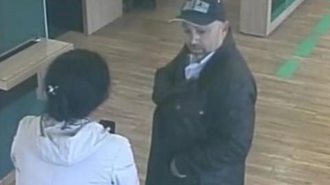 CCTV shot of the woman with her back to camera and the man wearing a baseball cap