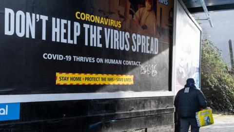 Man walking past Covid billboard