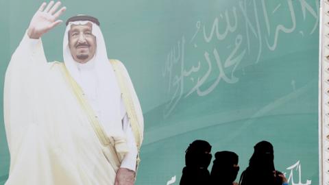 File photo showing women walking past a photo of Saudi Arabia's King Salman in Riyadh (12 February 2018)