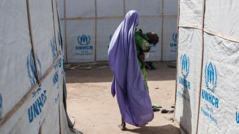 A woman carrying her baby walks through the temporary shelters provided by the Mission for the United Nations High Commissioner for Refugees (UNHCR) in one of the hosting communities in Maiduguri in northeastern Nigeria on December 7, 2016.