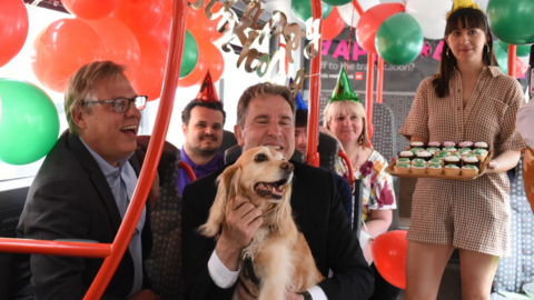 Dan Norris smiling and holding a dog while sitting on a bus decorated with balloons, birthday banners and cupcakes