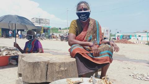 A woman fish vendor at a market in Tamil Nadu's Kattupalli covers her mouth with a mask that asks Adani Ports to stop its expansion plan