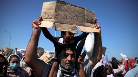 A child on a man's shoulder holds a sign reading: "We want freedom"