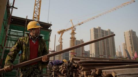 A worker carries a piece of steel at a construction site in Beijing