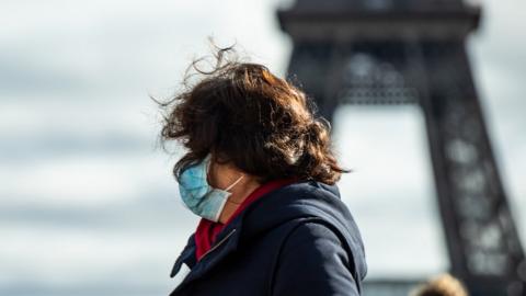 A tourist wears a face mark in front of the Eiffel Tower in Paris