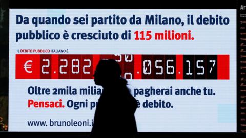 A woman walks past a "debt clock" screen in Milan