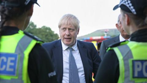 Prime Minister Boris Johnson meeting police during a visit to Whaley Bridge Football Club in Derbyshire, after the Toddbrook Reservoir near the village of Whaley Bridge was damaged in heavy rainfall