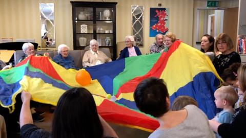 Residents at Ty Llandaff care home play with a parachute with mothers and toddlers