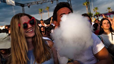 A festival-goer puffs a cloud of smoke from an electronic cigarette standing in a crowd of festival-goers in Cannes, south-eastern France, on 4 August 2023