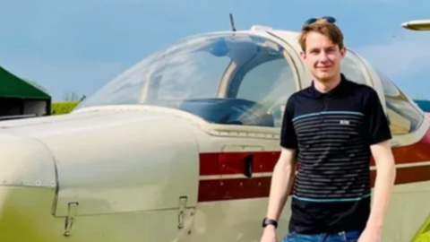 A young man stands next to a light aircraft