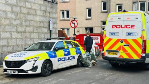 Police vans and cannabis plants outside a property.