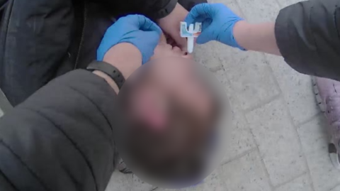 Bodycam still of naloxone being adminstered to a man whose face has been blurred