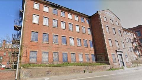 A Google Street View image of London Mill in Ashbourne Road, Leek. The building has at least four storeys and is made of red brick. The windows are square and Edwardian in style. 