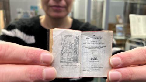 A close-up of a tiny bible showing the inside of the book. The picture shows a woman holding the book by her fingertips.