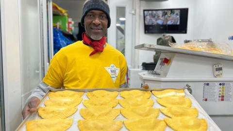 'Baker’ smiles as he holds up a tray of patties