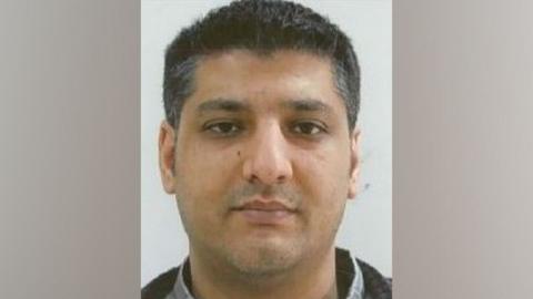 A mugshot of Baig, who has short salt and pepper hair and brown eyes. He looks straight at the camera.