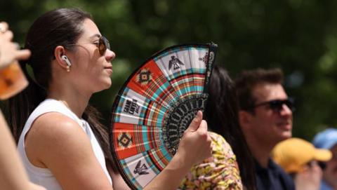 A woman in a white sleeveless top holds a fan