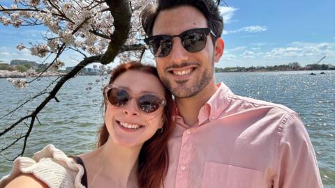 Yaron Lischinsky and Sarah Milgrim, both wearing sunglasses and smiling, with water in the background