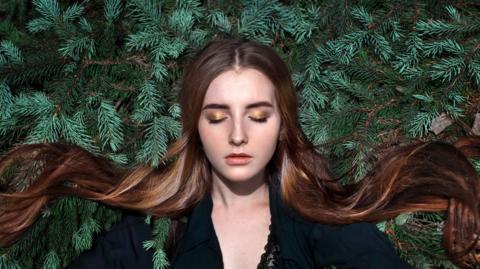 Woman surrounded by fern leaves closes her eyes