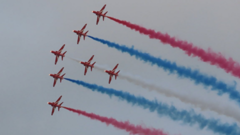The red arrows in the sky at the Guernsey Air Display. There are seven planes with red, blue and white smoke coming from them. 