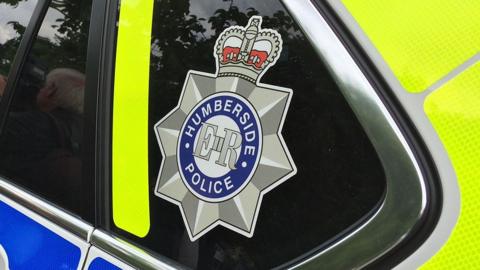 View of a marked yellow and blue Humberside Police car's rear side window which has the force's badge on it 