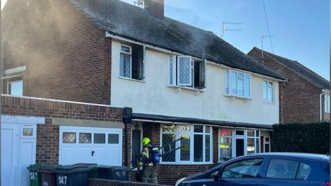 A firefighter entering a property which is damaged by fire. The firefighter is carrying a ladder.