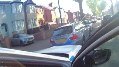 A blue car in an urban street seen from the door of a police vehicle