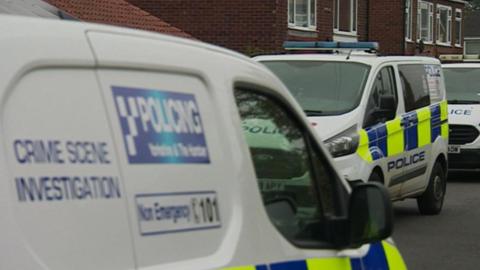 A close up of three crime scene investigation vans parked outside a row of houses.