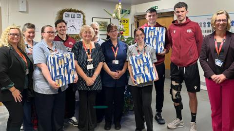 Football players standing with hospice staff. They are all smiling at the camera.