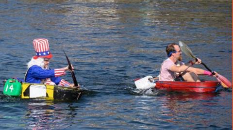 Two men paddling tin baths in the harbour, one is is fancy dress as Uncle Sam.