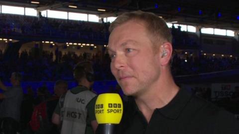 Sir Chris Hoy can be seen holding a yellow-branded 91ȱ Sport microphone. He is looking to the right of the camera, in conversation