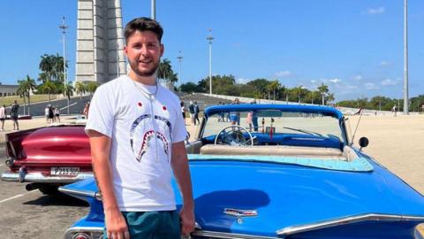 Danny Castledine stood in front of a car by a beach